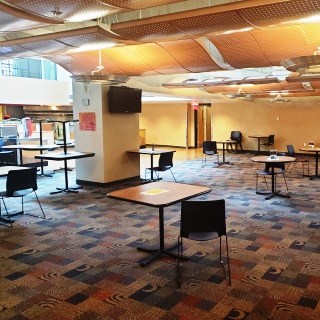 A cafeteria seating area with tables spaced far apart and one chair at each table.